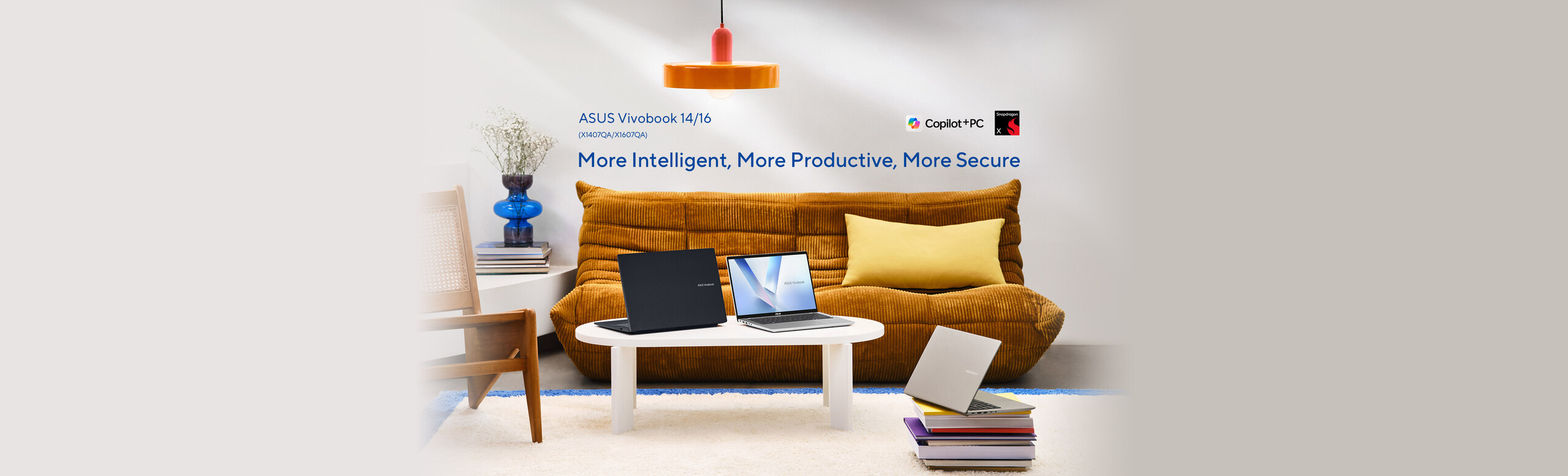 A silver and a black ASUS Vivobook laptop on a white table in front of an orange-coloured sofa